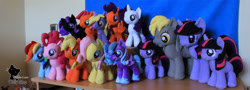 Size: 1938x700 | Tagged: safe, artist:wollyshop, applejack (mlp), derpy hooves (mlp), dinky hooves (mlp), fluttershy (mlp), pinkie pie (mlp), princess luna (mlp), rainbow dash (mlp), rarity (mlp), scootaloo (mlp), twilight sparkle (mlp), alicorn, earth pony, equine, fictional species, mammal, pegasus, pony, unicorn, feral, friendship is magic, hasbro, my little pony, clothes, feathered wings, feathers, female, filly, foal, folded wings, group, horn, irl, mare, photo, photographed artwork, plushie, shoes, smiling, tail, watermark, wings, young, younger